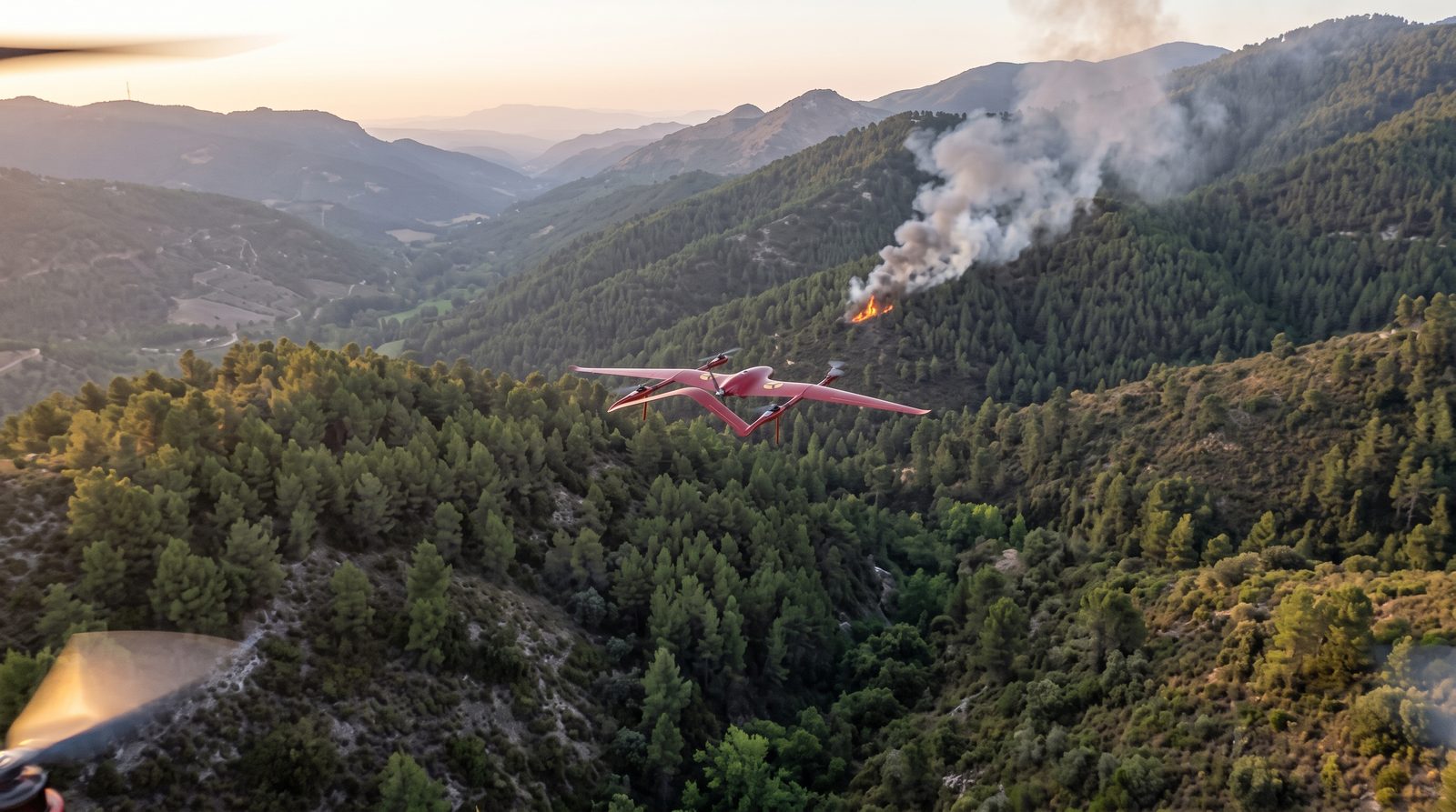 Fixed-wing VTOL drone flying over a forested hillside with a smoke plume and a fire in the background